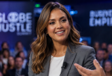 A realistic photograph of Jessica Alba wearing a tailored business blazer, smiling and speaking into a lapel microphone at a global corporate summit stage with an audience in the background.